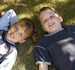 a young girl and boy laying in grass